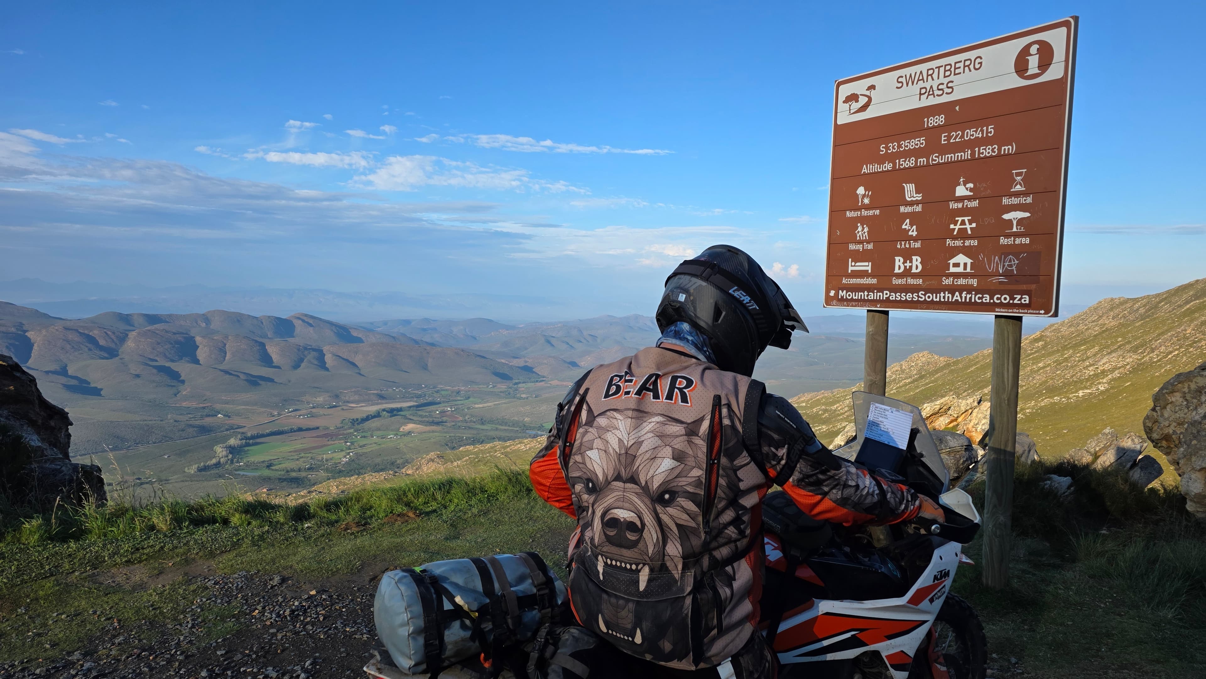 WillTour rider in MIRA gear on a KTM adventure bike at the Swartberg Pass summit, overlooking the Karoo valley.