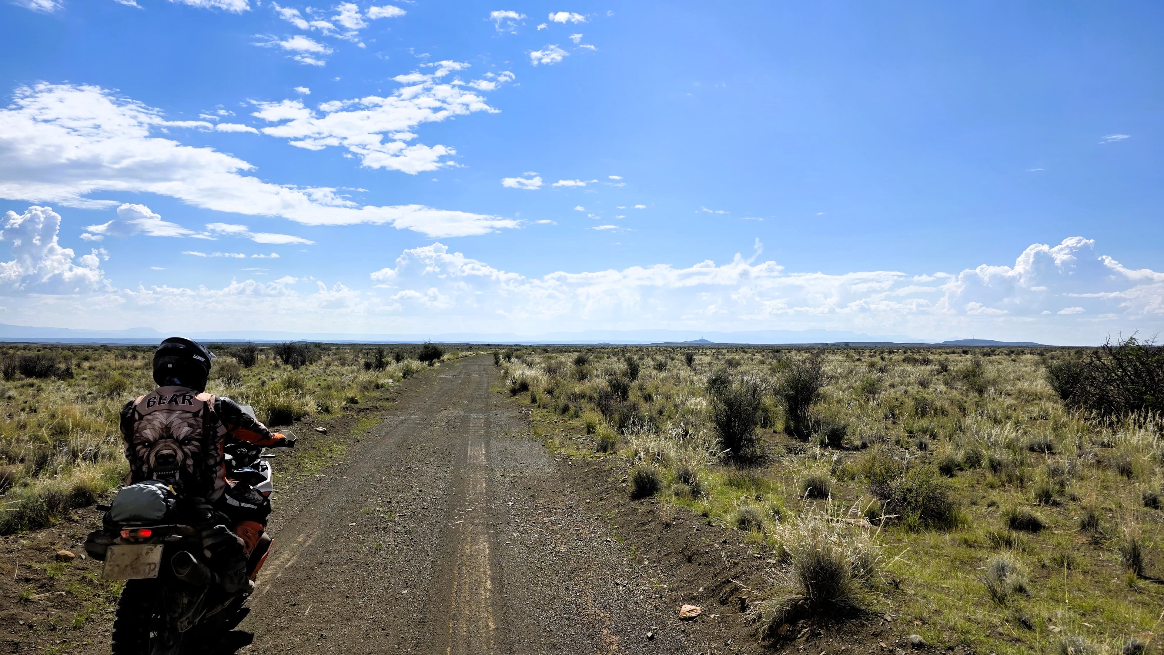 Adventure bike on a gravel road crossing the open Karoo plains under a wide blue sky on The Southern Arc.